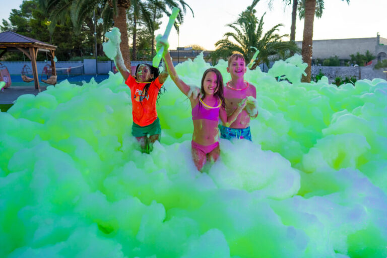 Kids playing in bubbly foam during an outdoor foam party rental event, hosted by Foam Fairies.
